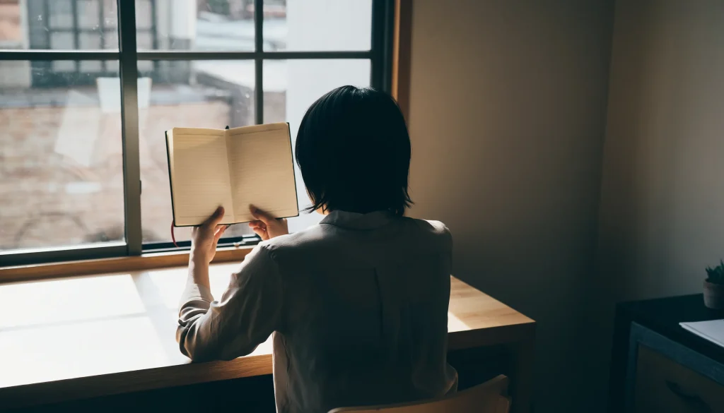 ADHDの悩みで自己否定に疲れている人が、静かな部屋でノートを開き考え込んでいる様子